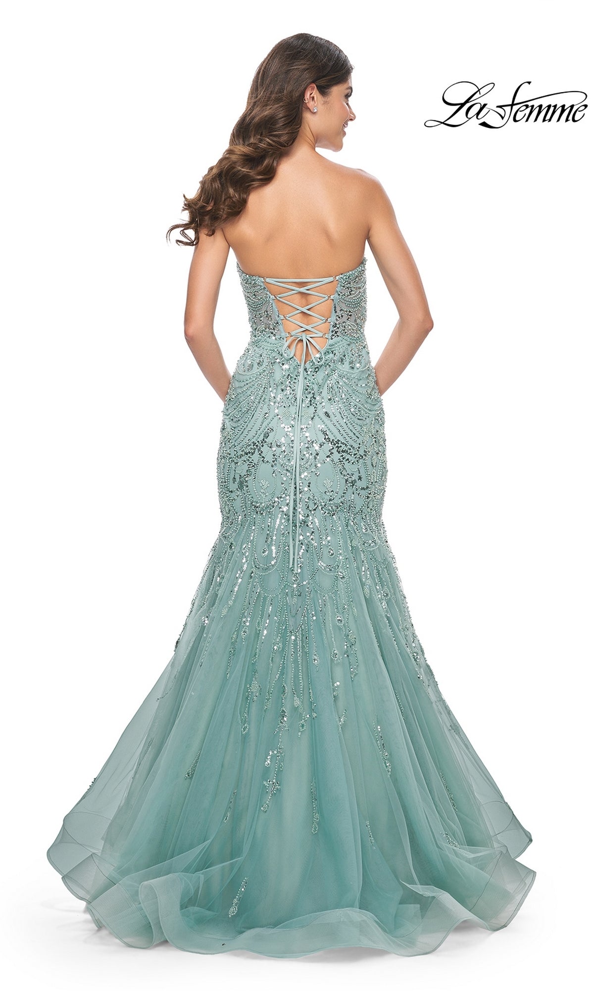 A woman stands with her back to the camera in the La Femme Strapless Long Mermaid Prom Dress 32053, a light blue gown with a sweetheart neckline, lace-up back, and sequin embellishments.